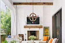 a lovely modern farmhouse outdoor living room with a fireplace, a suspended daybed, modern chairs, potted plants and blooms and a wooden chandelier
