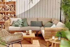 a lovely modern outdoor living room with a wooden deck, a planked sofa and a table, a rattan chair, a storage unit with firewood