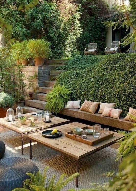 A modern Mediterranean outdoor living room with a built in bench, modern furniture, wicker ottomans and lots of greenery