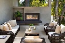 a modern outdoor living room with black wicker furniture, a concrete coffee table, a built-in fireplace and some potted greenery and a skylight