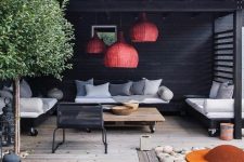a modern outdoor living room with red wicker lamps, modern furniture on casters, a fire pit with pebbles around and a tree
