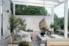 a neutral Scandinavian outdoor living room with olive green upholstered furniture, folding chairs and a coffee table, a pendant chair and potted plants