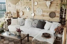 a neutral boho outdoor living room with a white corner sofa, a low coffee table, a gallery wall with mirrors and skulls and wovne pendant lamps
