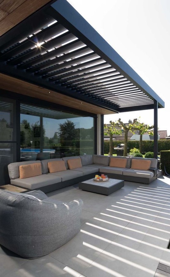 A simple modern outdoor living room under a beamed roof, an L shaped sofa, a beanbag chair and a coffee table