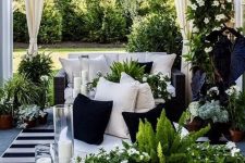 a stunning black and white outdoor living room with black wicker furniture, a stone bench, lots of greenery, blooms and candles