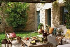 a welcoming Mediterranean outdoor space with a neutral sofa with bright pillows, a stained wooden table, greenery and blooms and candle lanterns is amazing