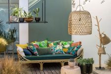a welcoming tropical outdoor living room with a rattan sofa, colorful pillows, a jute rug, wicker baskets and a wicker lampshade plus potted plants