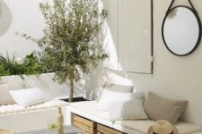 a white Mediterranean terrace with built-in benches, greenery and a tree, crates for storage and a small roof