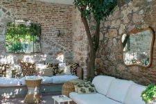 an outdoor living room with stone and brick walls, wicker and wooden furniture and greenery