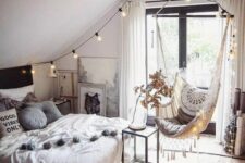 a boho teen attic bedroom with a bed with neutral bedding, a woven pendant chair, lights, wooden beams and artwork
