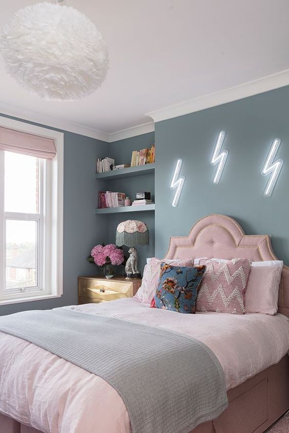 a pastel teen bedroom with blue walls, a pink bed with pastel bedding, built-in shelves, a stained dresser and blush curtains