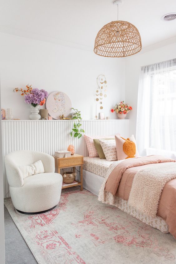 a vivacious teen girl bedroom in neutrals with a paneled shelf with blooms and art, a bed with printed bedding, a white chair and a woven pendant lamp