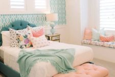 a bright teenage bedroom with a turquoise upholstered bed and a matching accent wall, a peachy ottoman and pillows