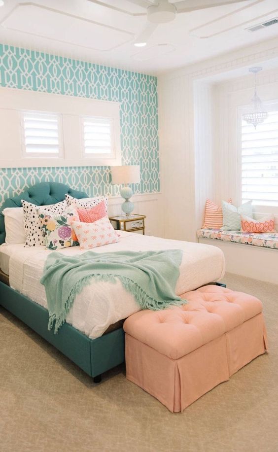 a bright teenage bedroom with a turquoise upholstered bed and a matching accent wall, a peachy ottoman and pillows