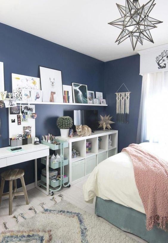a contemporary teen bedroom with storage units from IKEA, a white desk, an open shelf, navy walls and a comfy bed