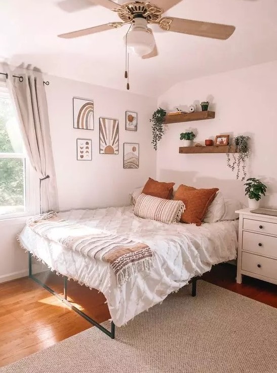 A boho teen bedroom with a metal bed, a gallery wall, wall mounted shelves, a white dresser, potted greenery and neutral textiles
