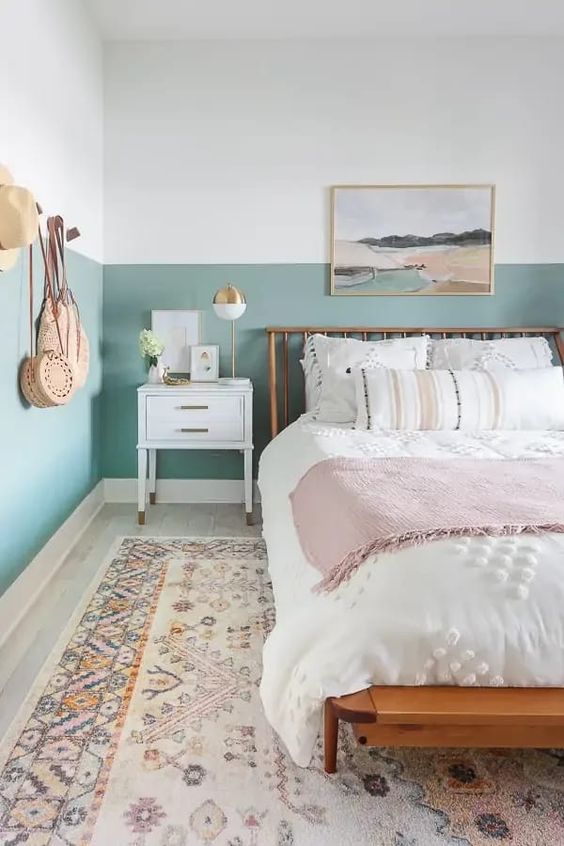 a boho teen bedroom with color block walls, a wooden bed with neutral bedding, a printed rug, an artwork is cool