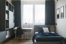 a chic contemporary teen boys room with a large storage unit taking one wall, a small desk and a comfy bed, a gallery wall and blue curtains