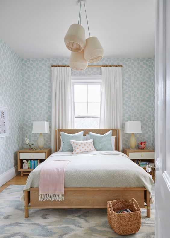 a lovely and peaceful teen bedroom with blue wallpaper, a stained bed with pastel bedding, stained nightstands, pendant lamps