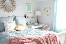 a welcoming teen bedroom with a small vanity and desk, a white bed with blue bedding, blue curtains, a sunburst mirror
