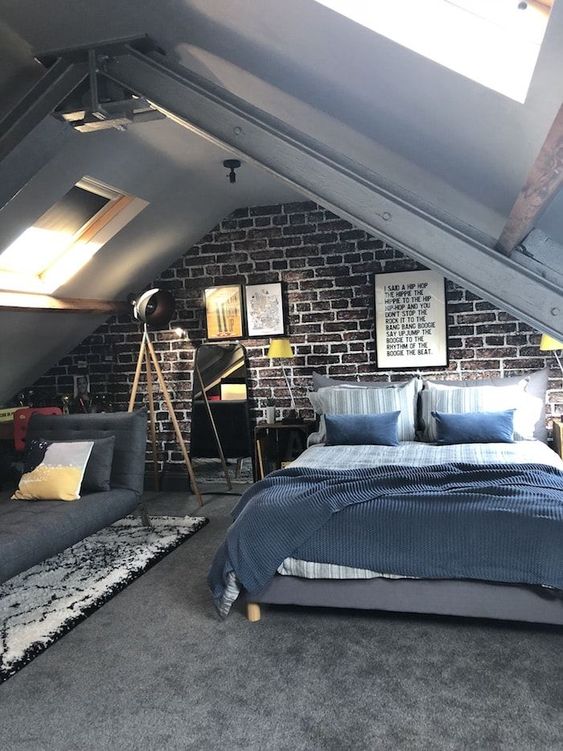 an attic teen bedroom with a brick accent wall, a bed with blue bedding, a grey sofa, a printed rug and some posters
