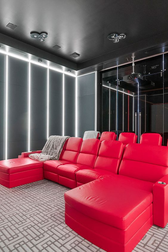 A bold modern home theater with grey walls with built in lights, hot red seating furniture, a glazed wall and a black ceiling