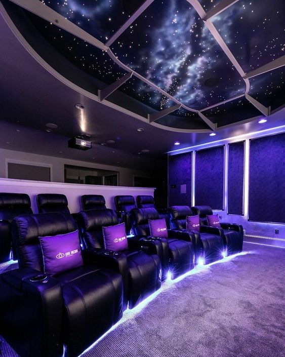 A jaw dropping home theater with deep purple walls and a starry sky ceiling, black leather chairs, built in lights is a chic space