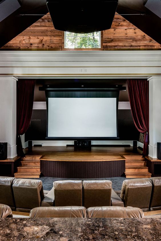 a luxurious and chic home theater with stained walls and leather seating furniture, burgundy velvet curtains and chair covers
