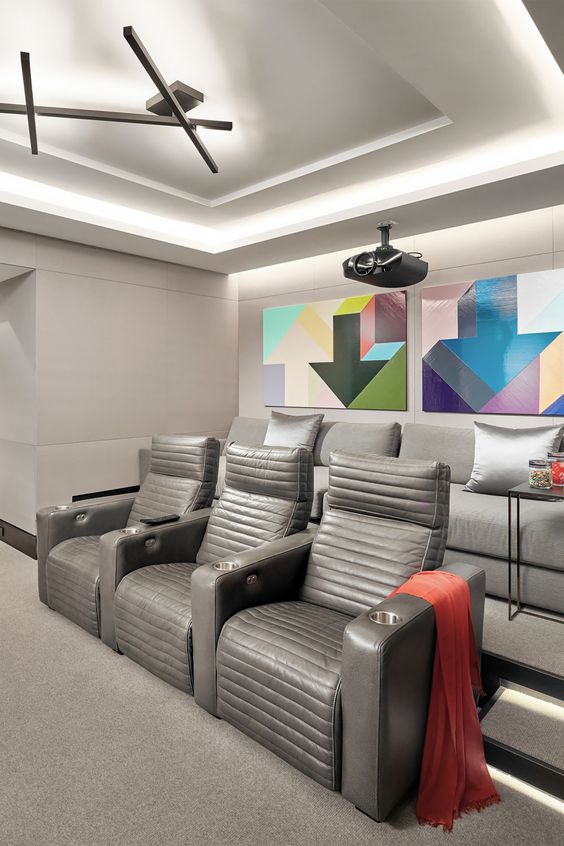 A modern home theater in greys, with grey seating furniture, colorful geometric artwork and built in lights is a cool space