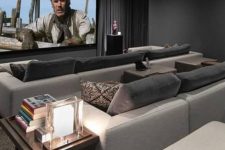 a modern home theater with graphite grey walls, neutral sofas and grey pillows, a large screen, built-in lights and a side table