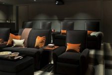 a moody home theater with graphite grey walls and a ceiling with built-in lights, black chairs and sofas, bright pillows