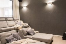 a neutral and comfortable home theater with grey seating furniture, grey walls, neutral textiles and elegant sconces and built-in lights