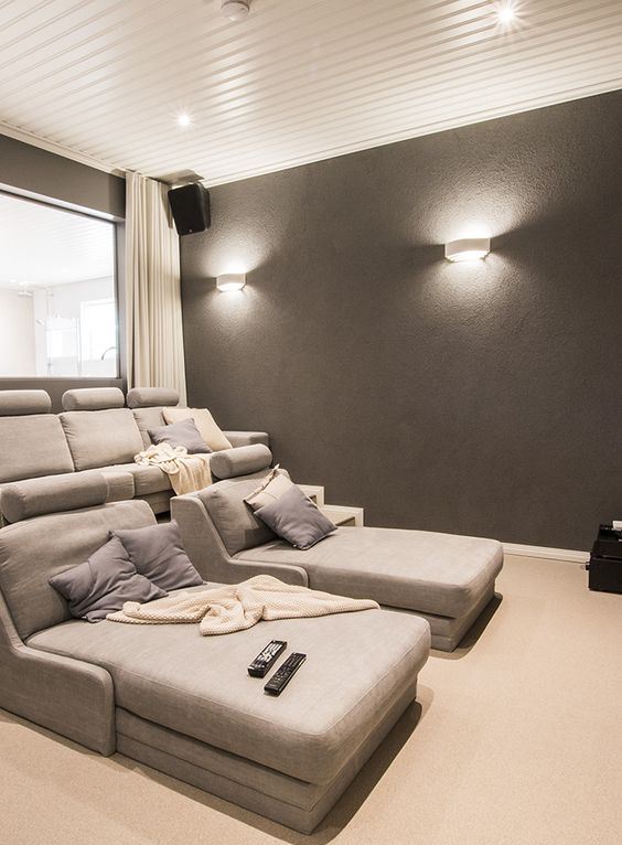 A neutral and comfortable home theater with grey seating furniture, grey walls, neutral textiles and elegant sconces and built in lights
