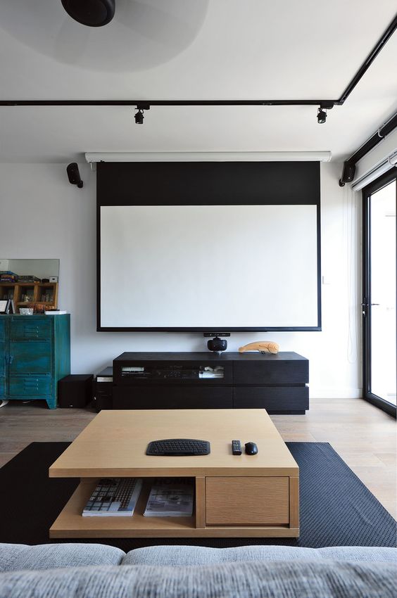 a simple and laconic home theater with a glazed wall, a screen, a black media console, a stained coffee table and a grey sofa plus lots of lights