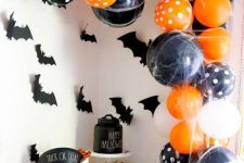 a bold Halloween dessert table with orange, black and white balloons, bats, cauldrons with sweets