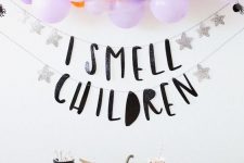 a catchy Halloween party space with lilac balloons, witches’ hats, printed cups and plates and a banner