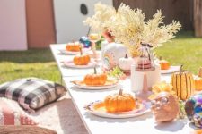 a colorful Halloween kids’ party table setting with dried leaves, pastel skulls, pumpkins and a pink rug to sit on
