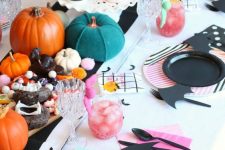 a colorful Halloween party table with mint and pink napkins, striped and bat plates, colorful pumpkins and delicious cupcakes