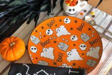 a colorful Halloween place setting with a bright orange plate, a black napkin, a bold pumpkin and some feathers