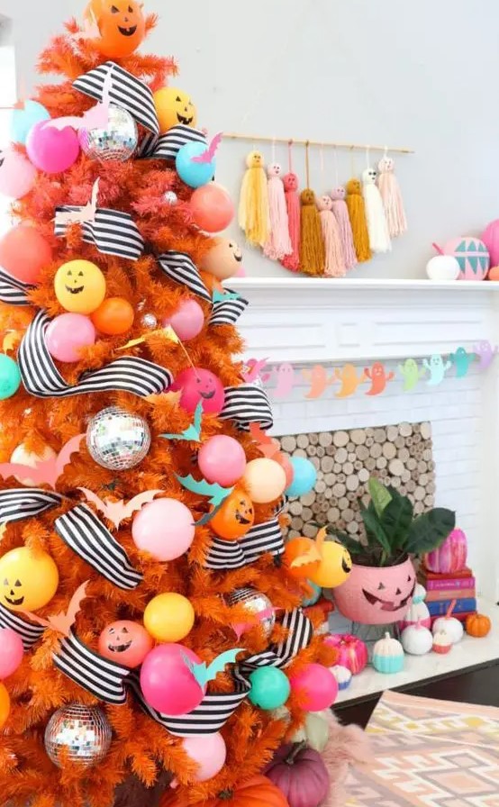 A colorful Halloween tree in orange, with pastel ornaments and balloons, striped garlands and jack o lanterns
