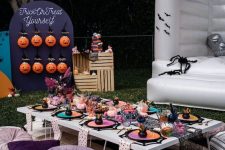 a lovely Halloween party table with colorful plates, cushions on the ground and pumpkins with popcorn