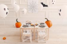 a lovely kids’ Halloween party space with ghost balloons, bats, pumpkins and a black and white tablescape done with cheesecloth