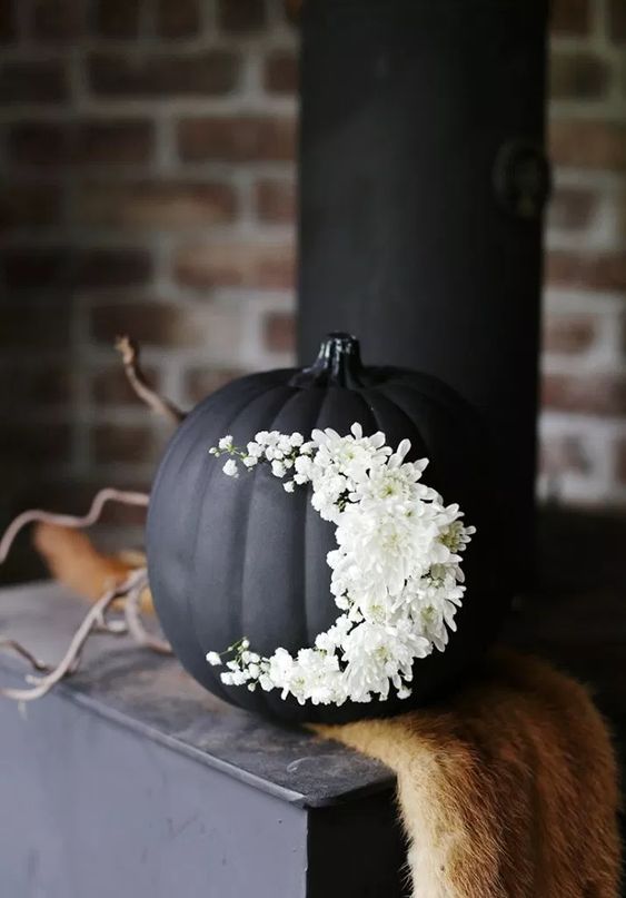 a matte black pumpkin decorated with white flowers is a very chic and beautiful Halloween decor idea