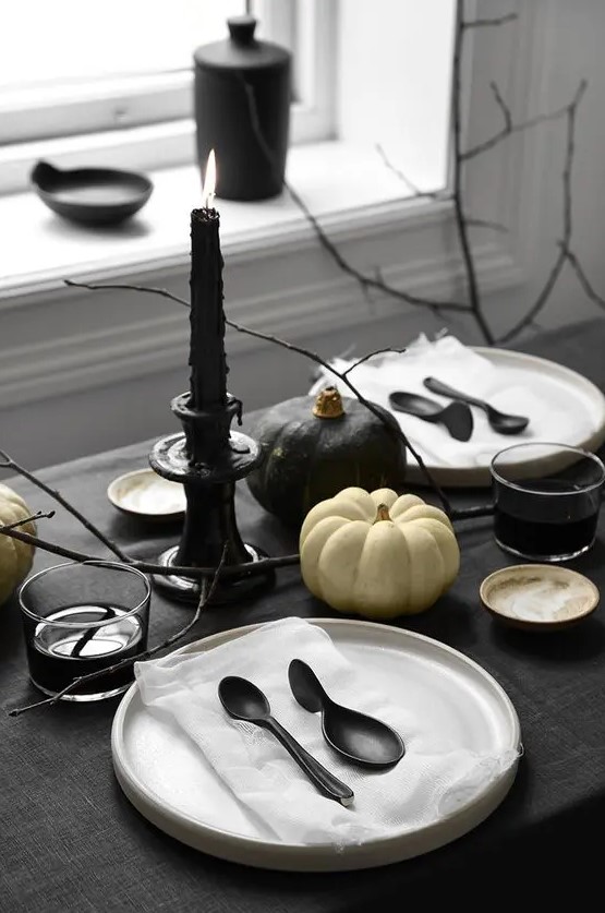 a minimalist Halloween table setting with black and white linens, black cutlery and candles, black and white pumpkins