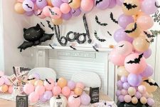 a pastel Halloween party space with a cauldron with orange, blush and lilac balloons, matching ones on the table and some lovely plates
