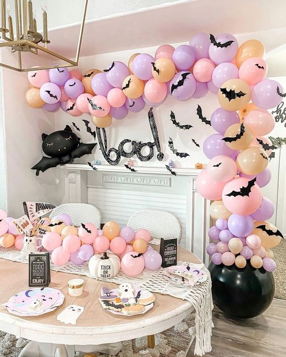 a pastel Halloween party space with a cauldron with orange, blush and lilac balloons, matching ones on the table and some lovely plates