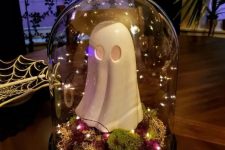 a simple Halloween cloche with moss, bold dried blooms, lights and a funky ghost figurine is a cool idea for a kids’ party