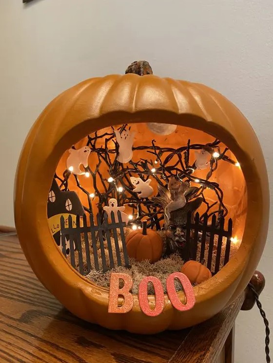 an orange pumpkin with hay, a fence, a paper house, ghosts attached to the lights and small pumpkins