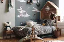 a Nordic kid’s bedroom with an accent corner, a wooden house-shaped bed with printed bedding, layered rugs, buntings and racks