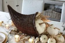 a Thanksgiving centerpiece of a woven cornucopia, white pumpkins, wheat and gilded nuts is a gorgeous idea for your party table